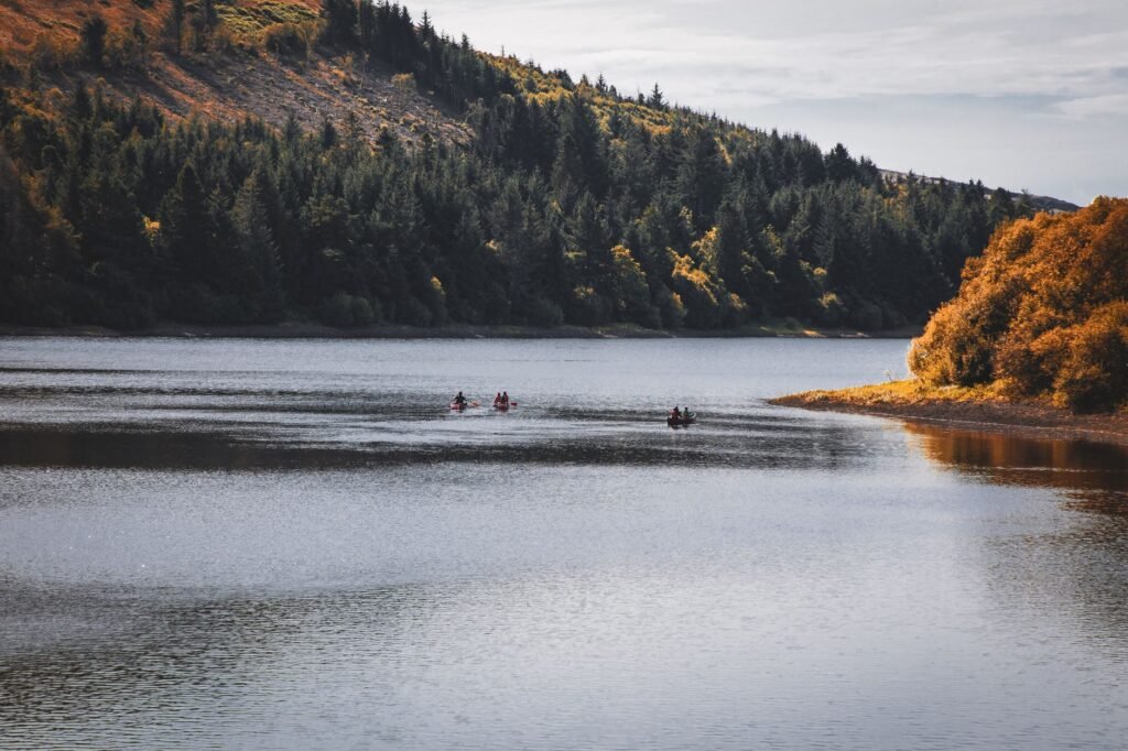 Canoe on a serene lake in Brecon Beacons, Wales with forested hills in fall colors.
