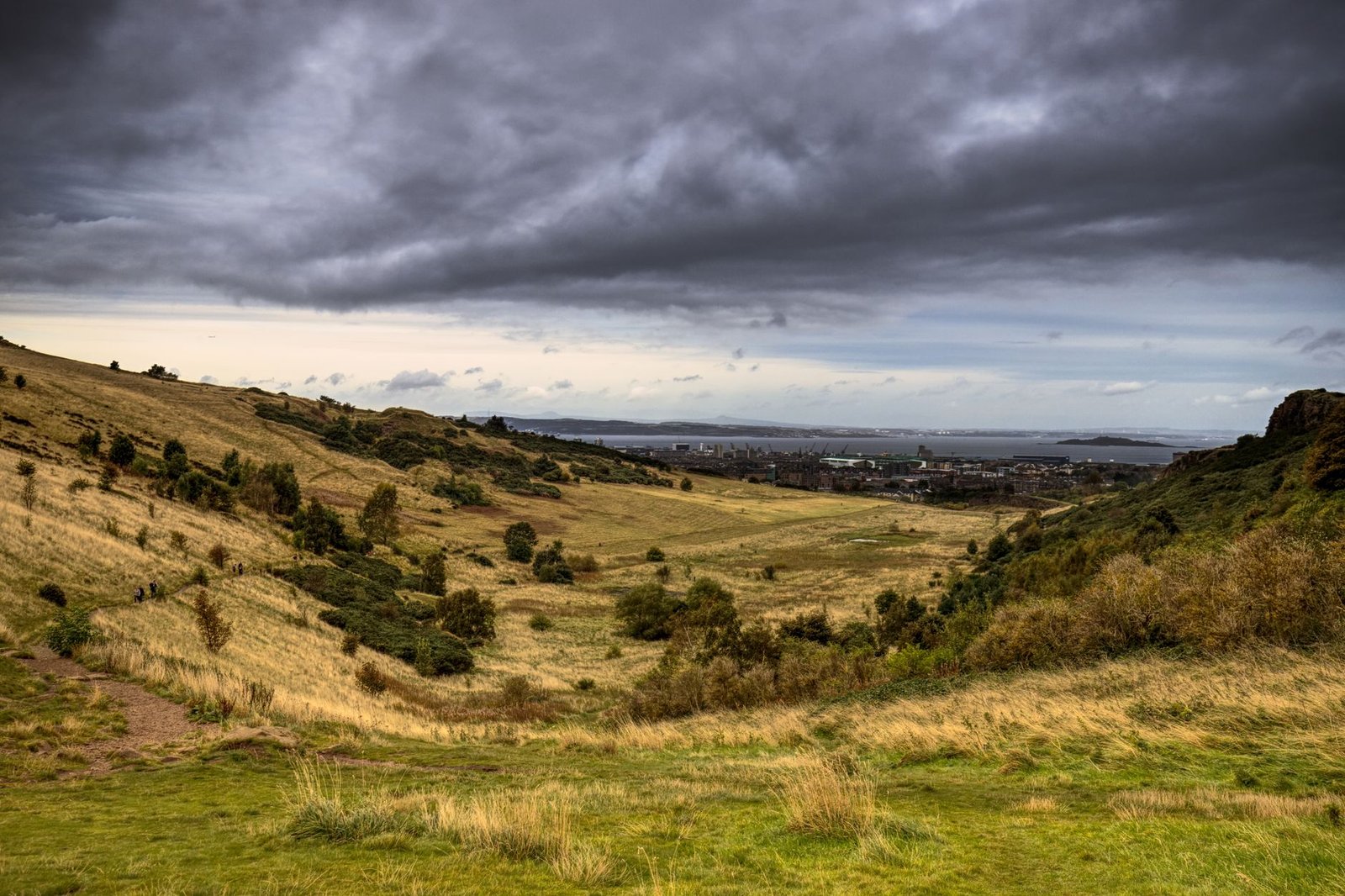 Explore the vast grassy fields in Scotland under a dramatic cloudy sky.