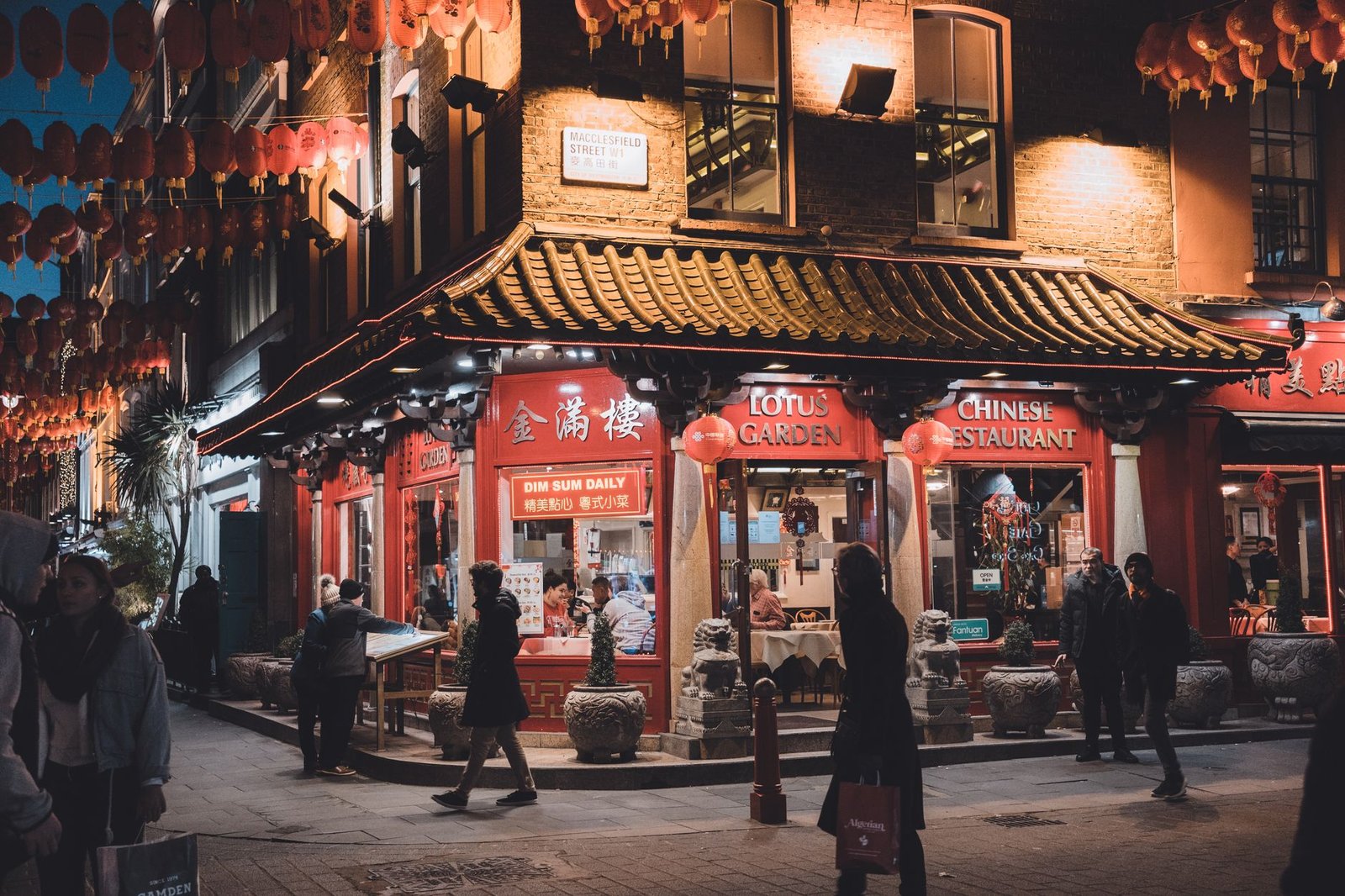 A vibrant night scene of lively Chinatown in London, featuring a traditional Chinese restaurant illuminated by red lanterns.