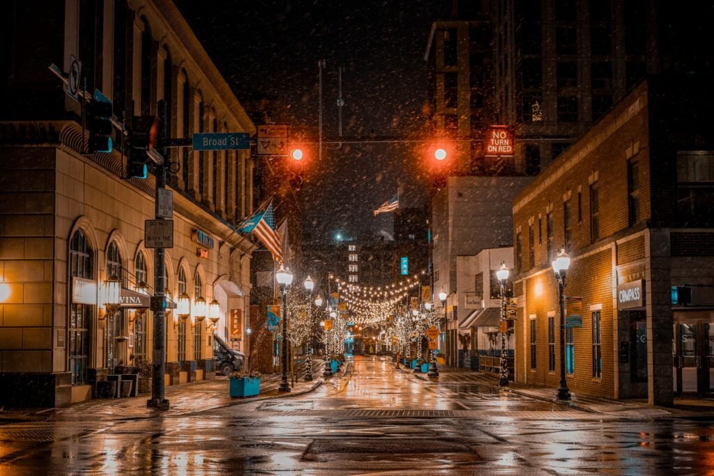 A beautifully lit street in Stamford at night during snowfall, showcasing holiday decorations.