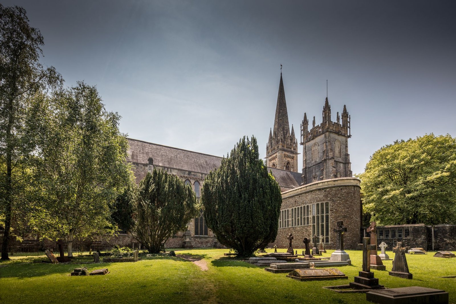 Historic Llandaff Cathedral surrounded by lush greenery and gravestones in Wales.