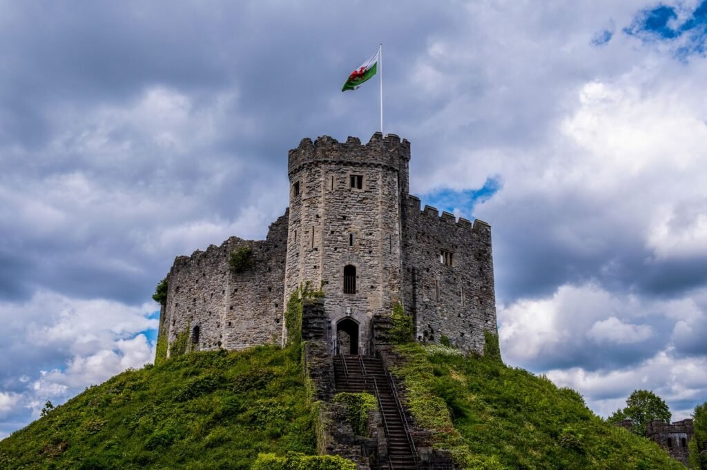 Majestic Cardiff Castle in Wales, topped by a flag, under dramatic cloudy skies.