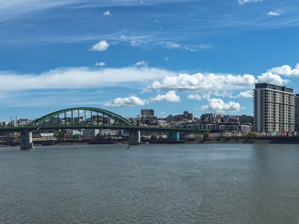 Cityscape of Belgrade featuring the Old Sava Bridge and river, with modern architecture.