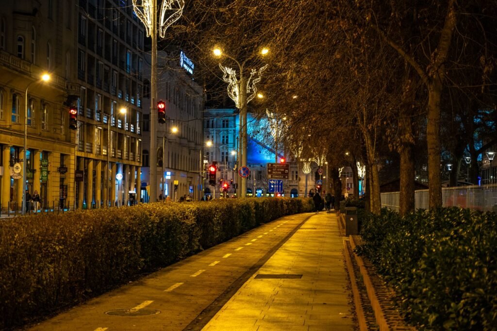 Illuminated street in Budapest, Hungary at night with festive decorations and pedestrian path.