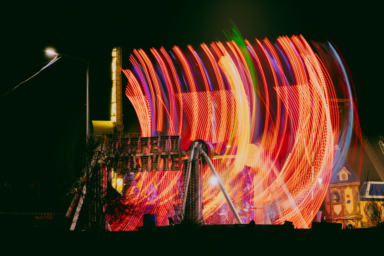 A colorful night scene captures vibrant neon lights creating stunning motion trails at an amusement park.
