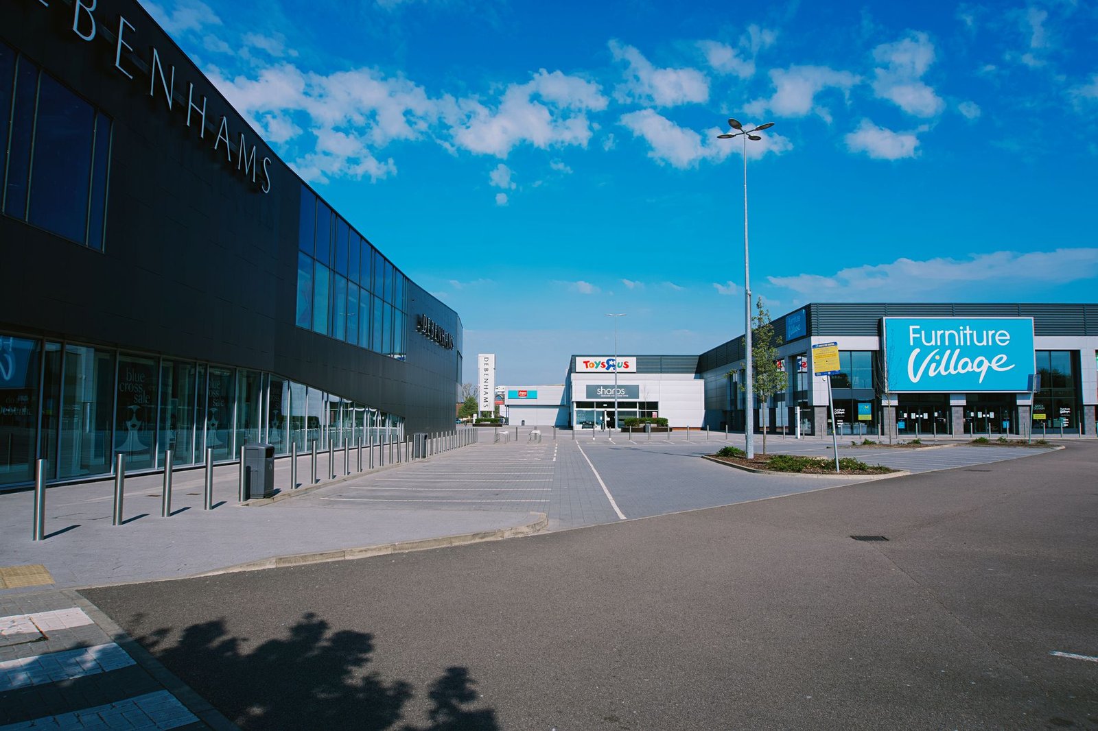 A modern shopping mall exterior in England with large signs and parking area.