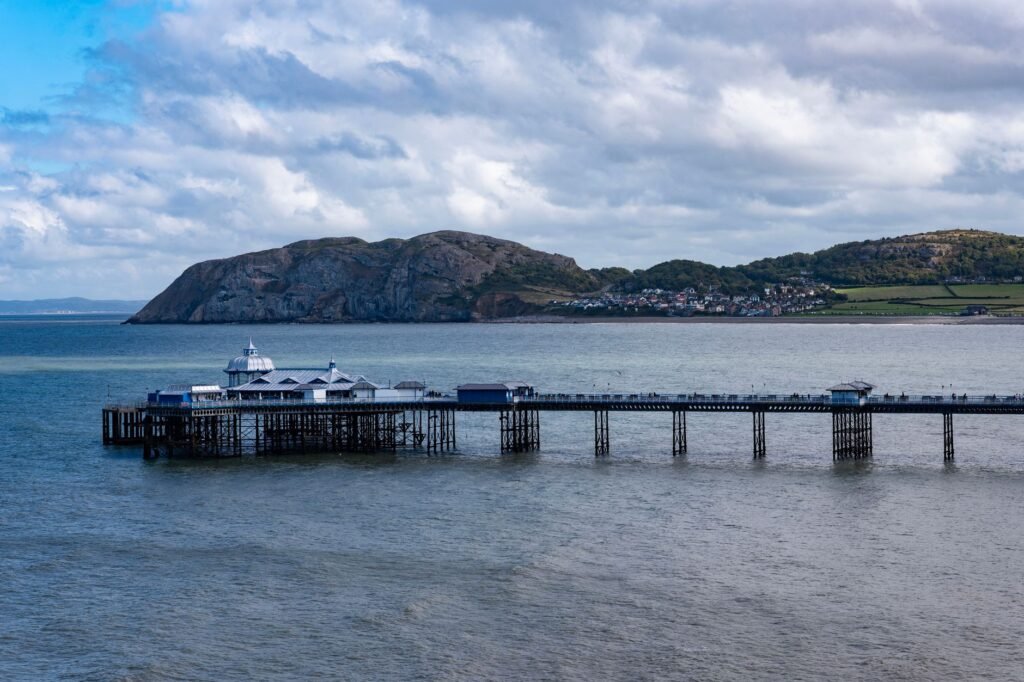 A beautiful view of Llandudno Pier stretching into the sea with a stunning backdrop of hills and clouds.