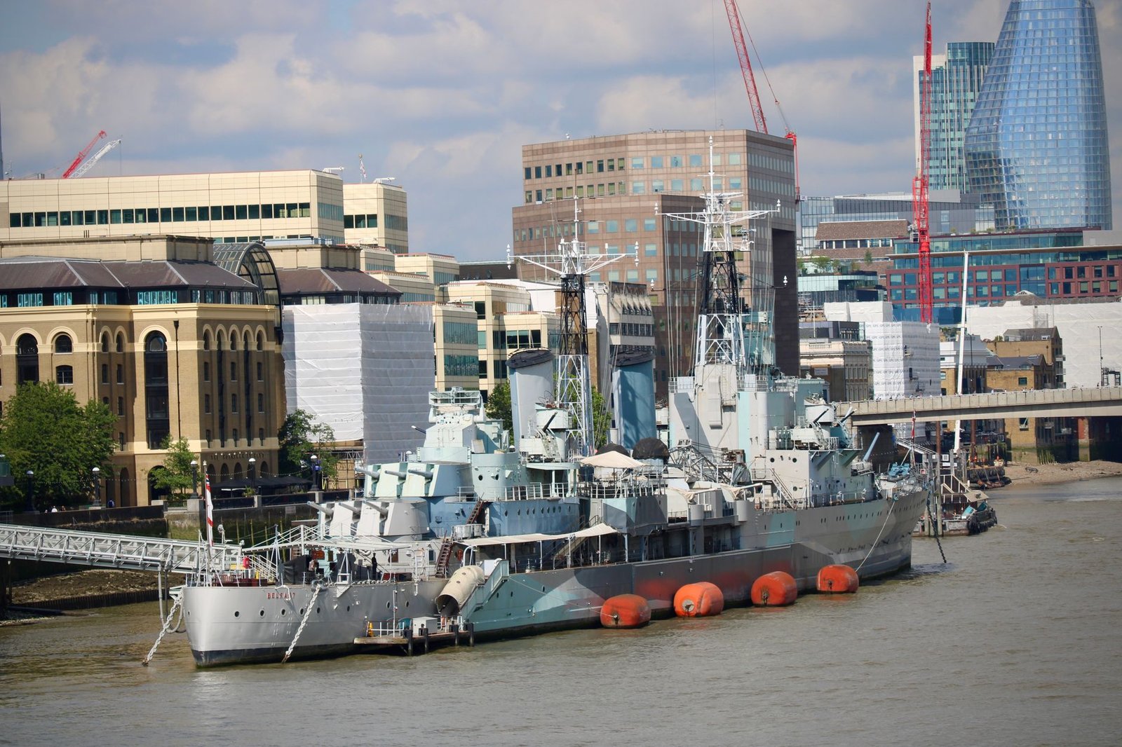 HMS Belfast stationed on the River Thames with London's skyline in the background.