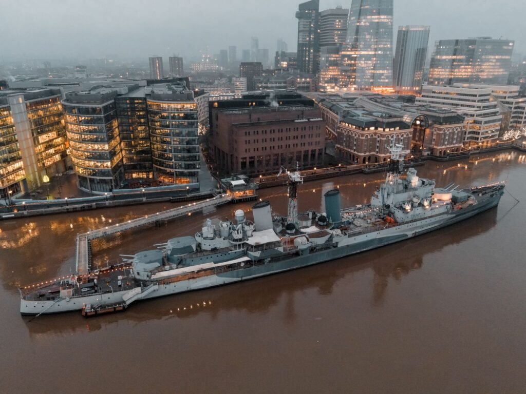 Aerial shot of the iconic HMS Belfast moored on the Thames against London's illuminated skyline at dusk.