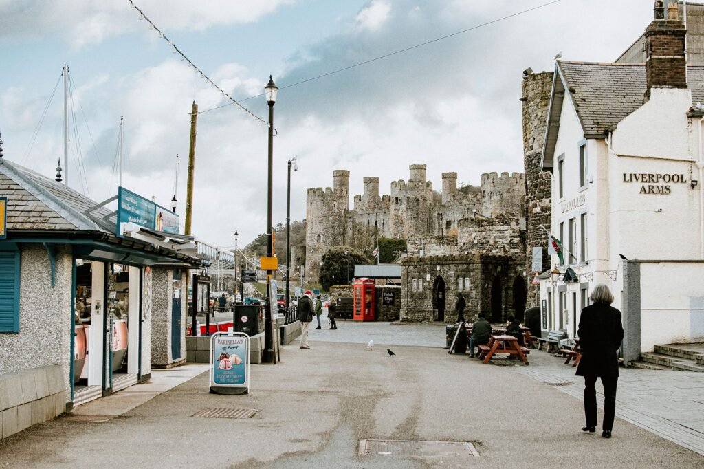 Street scene with Conwy Castle, shops, and pedestrians in Wales, UK.