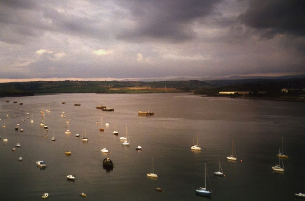 Aerial view of various sailboats peacefully anchored on a calm sea in the UK under a cloudy sky.