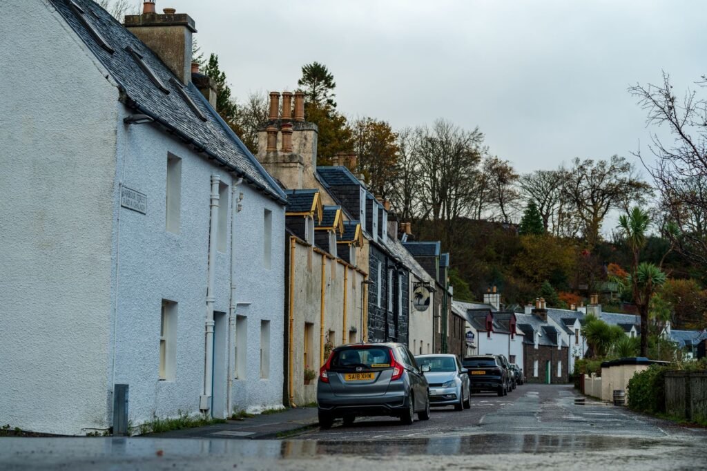 A picturesque street in a Scottish village lined with traditional stone cottages and parked cars.