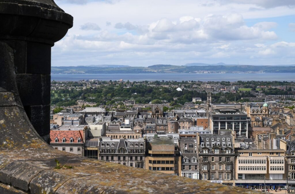 Panoramic view of Edinburgh skyline from historic location, showcasing architecture and distant seascape.