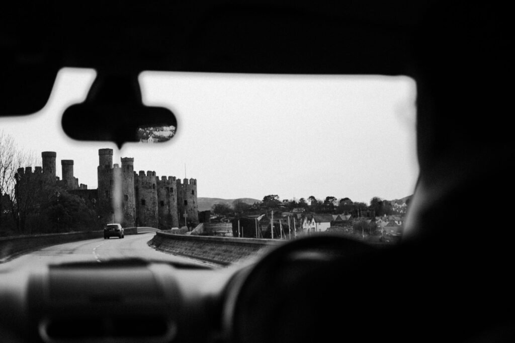 A black and white view from a car interior driving past a historic castle.