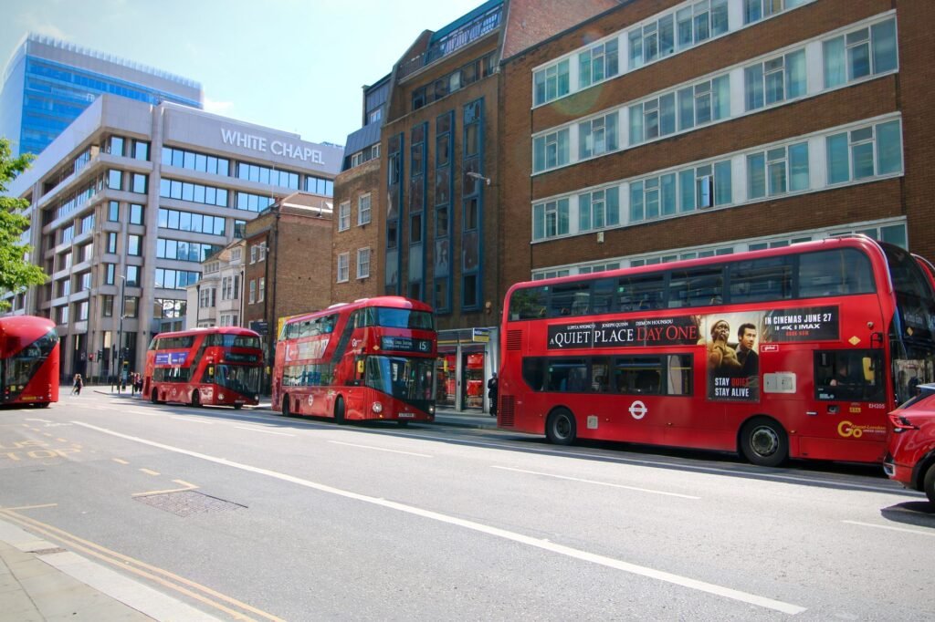 Red double-decker buses on a sunny day in Whitechapel, London, with city street and buildings.