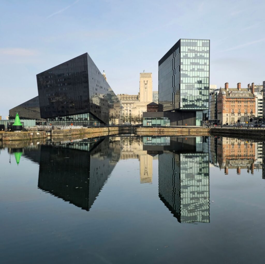 Stunning modern architecture reflecting in Liverpool's iconic waterfront under clear skies.