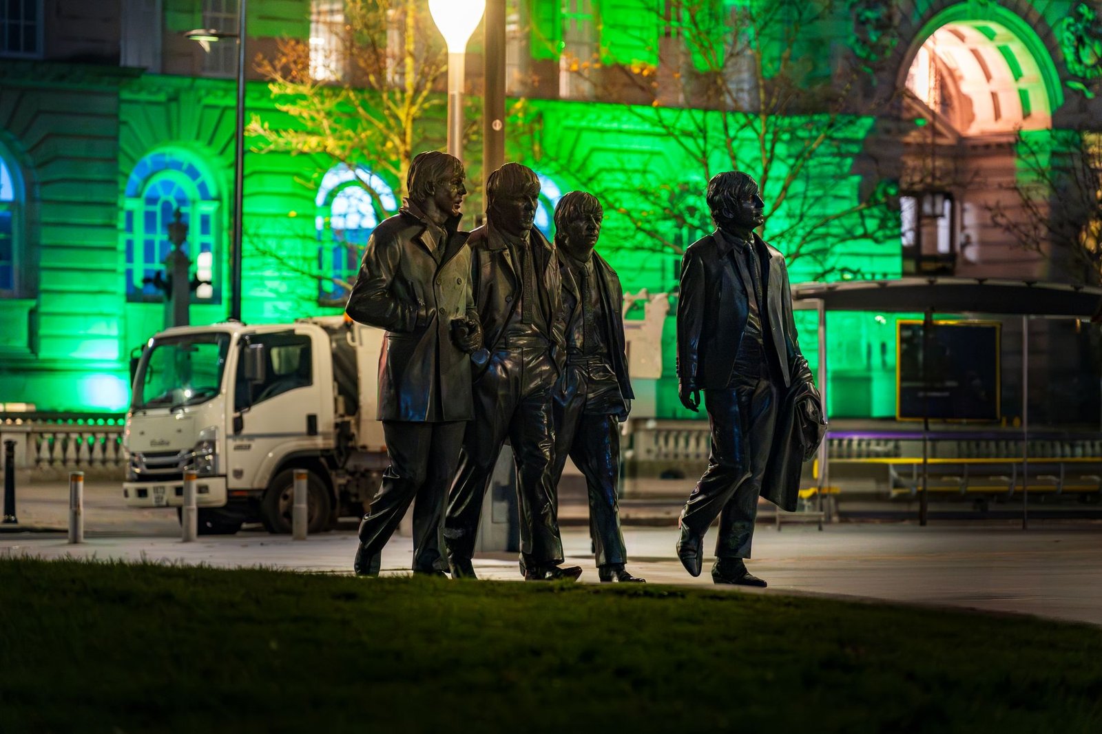 Nighttime shot of the famous Beatles statue in Liverpool, UK, with vibrant green lighting.
