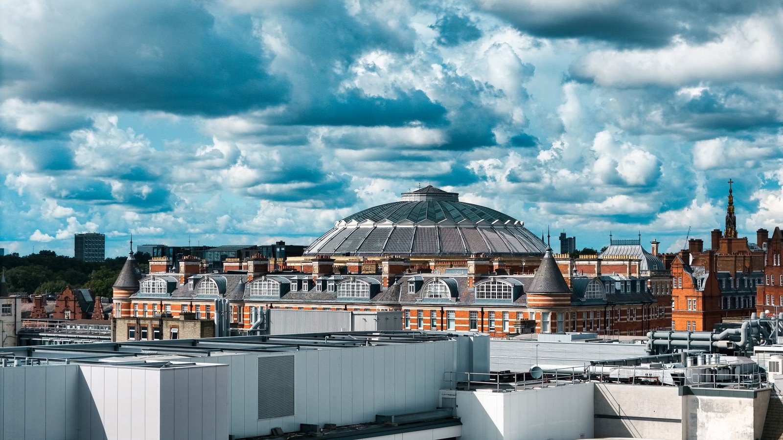 A vibrant view of the Royal Albert Hall in London under a dramatic cloudy sky.