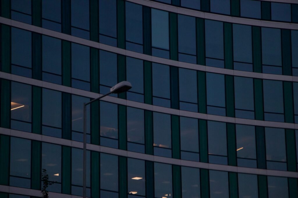 Curved glass facade of an urban office building with street light at twilight.