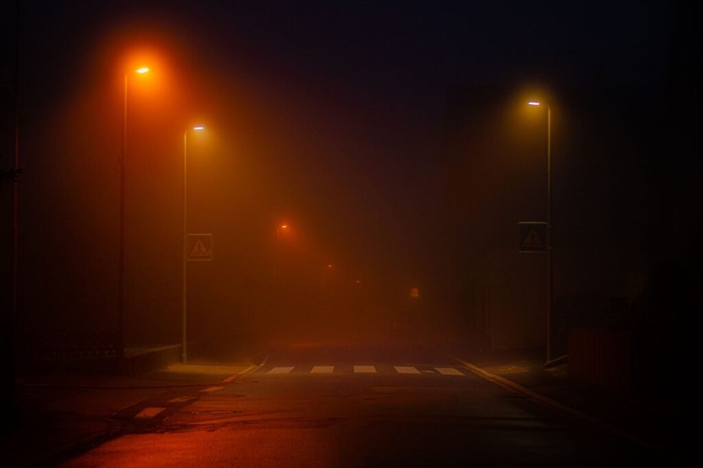 A foggy street scene illuminated by streetlights, creating a mysterious atmosphere.