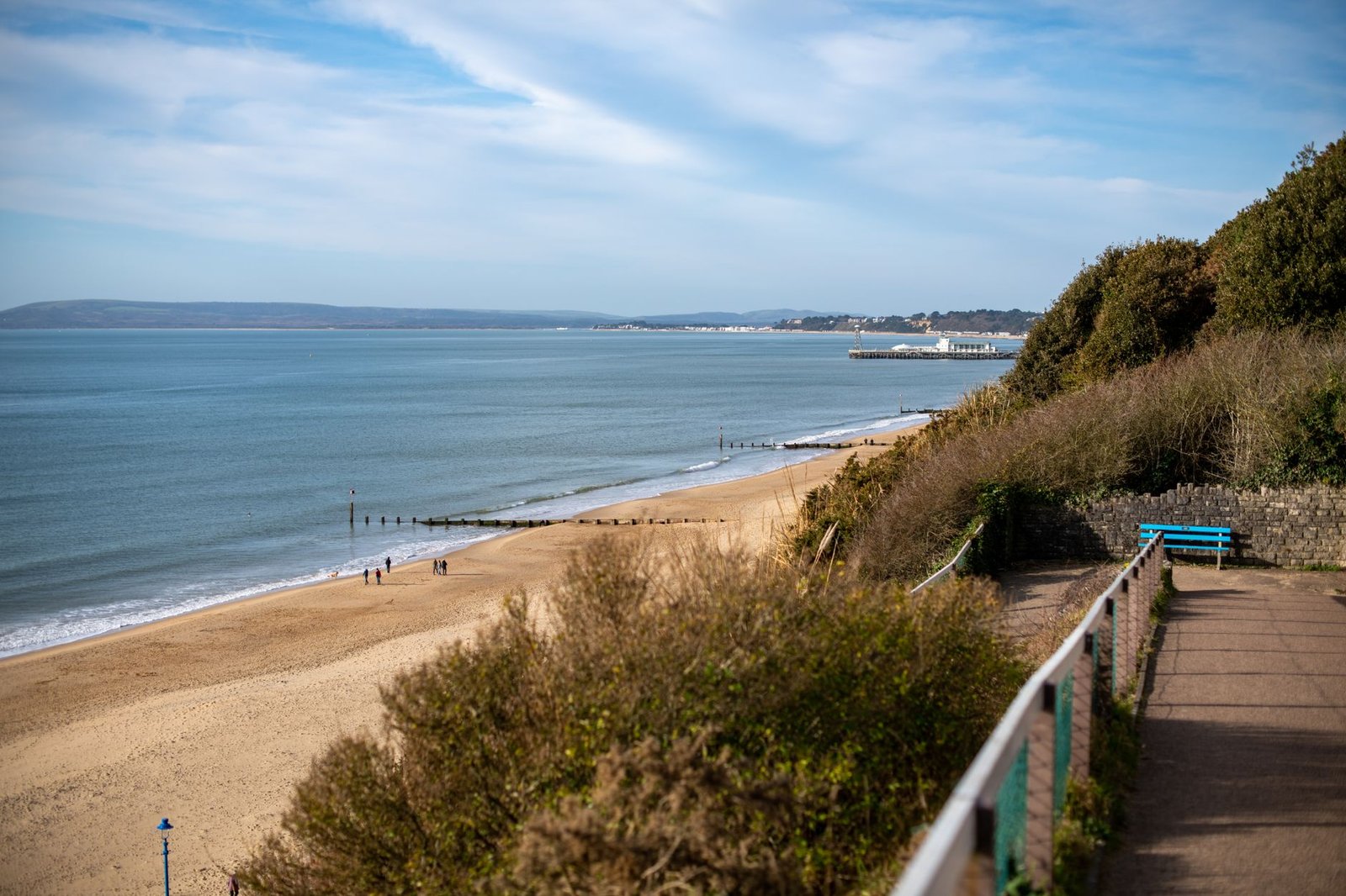 A picturesque view of a coastal pathway overlooking a sandy beach and calm sea on a clear day.