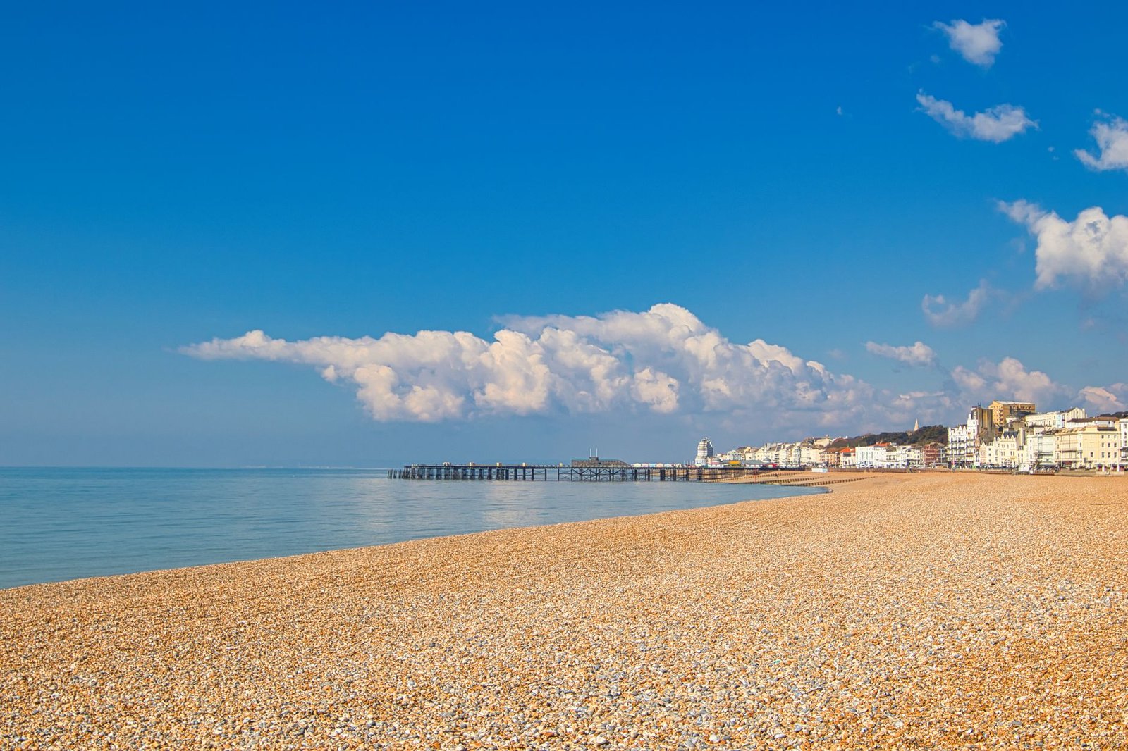 A serene pebble beach with a clear blue sky and a quaint coastal town in the background.