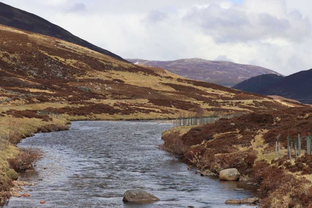 Scenic view of a river flowing through the Scottish Highlands, surrounded by hills.