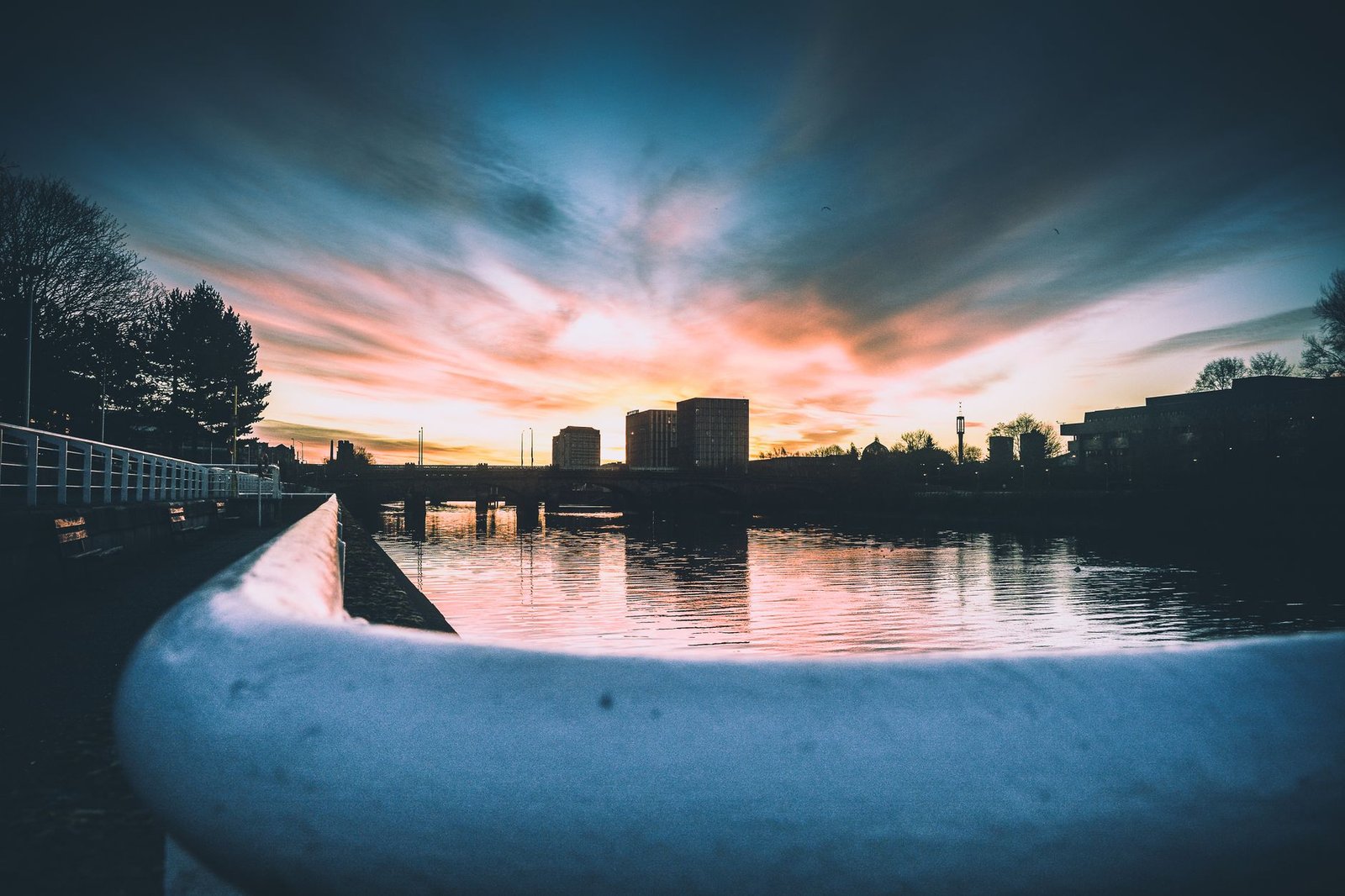 Breathtaking view of a sunset casting vibrant hues over a city's skyline, reflected in serene river water.