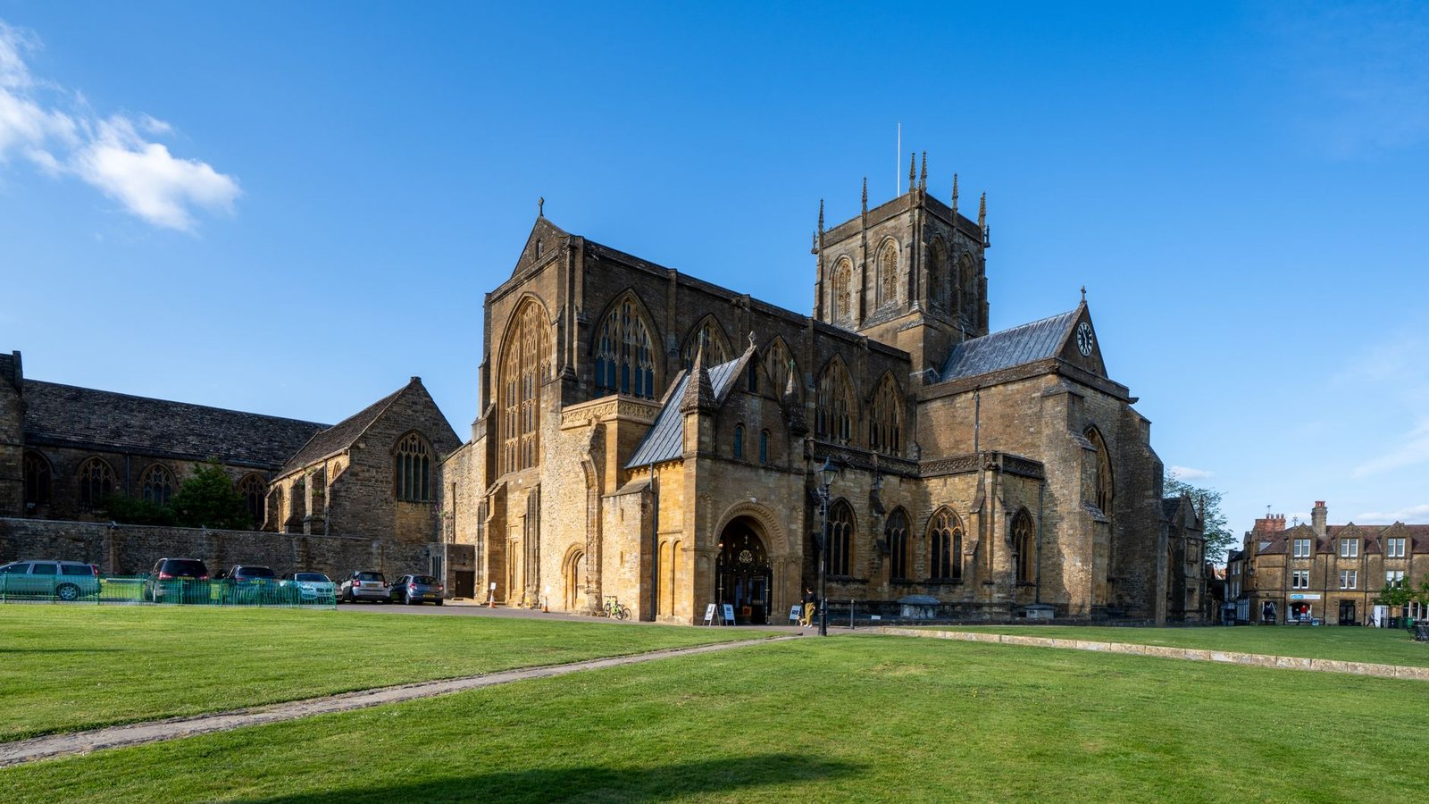 A stunning view of a historic abbey church with gothic architecture in the English countryside, under a clear blue sky.