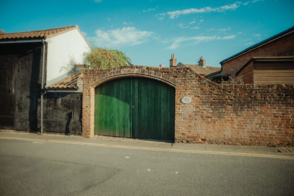 Vintage brick gate with a green door on a quiet street in Dereham, England.