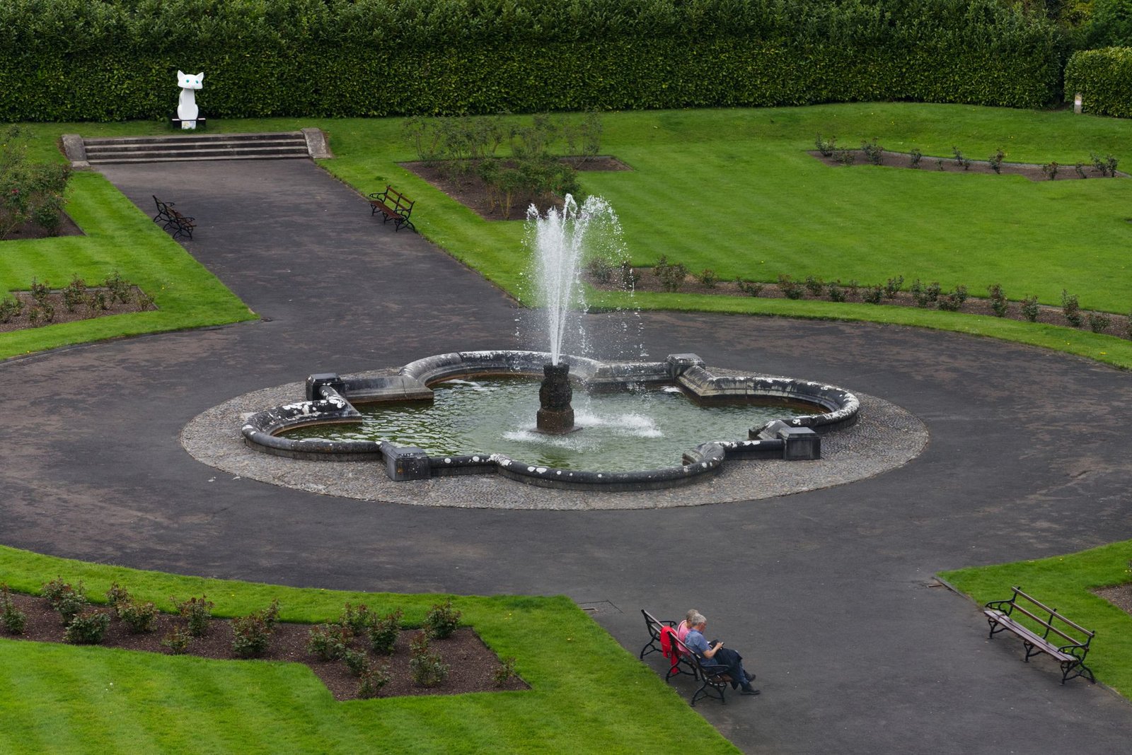 Aerial view of a tranquil park with a central water fountain surrounded by lush greenery.