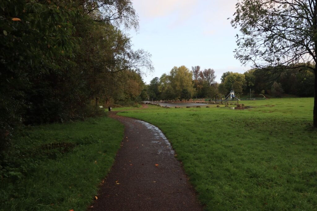 A serene park path in England surrounded by lush greenery during sunset.