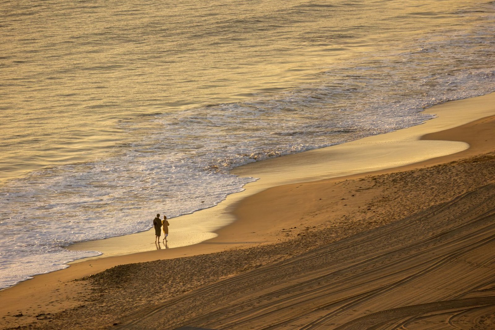 A couple strolls along a tranquil beach with gentle waves at sunset creating a romantic ambiance.