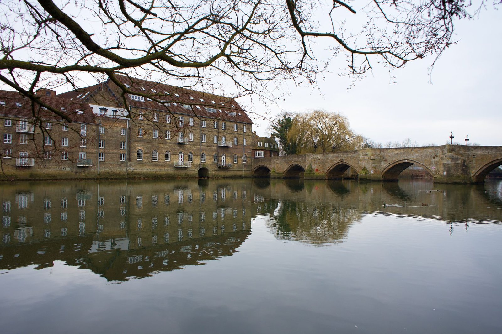 Serene view of historic bridge and buildings reflecting in the River Great Ouse in Godmanchester, England.