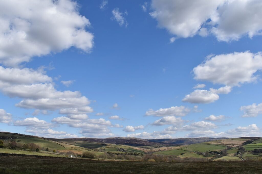 Serene rural landscape in England with rolling hills and scattered clouds under a clear blue sky.
