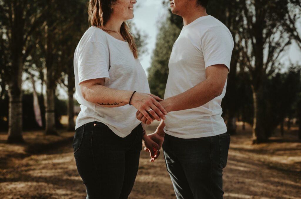 A couple in casual attire holds hands in a sunlit park, creating a romantic outdoor moment.