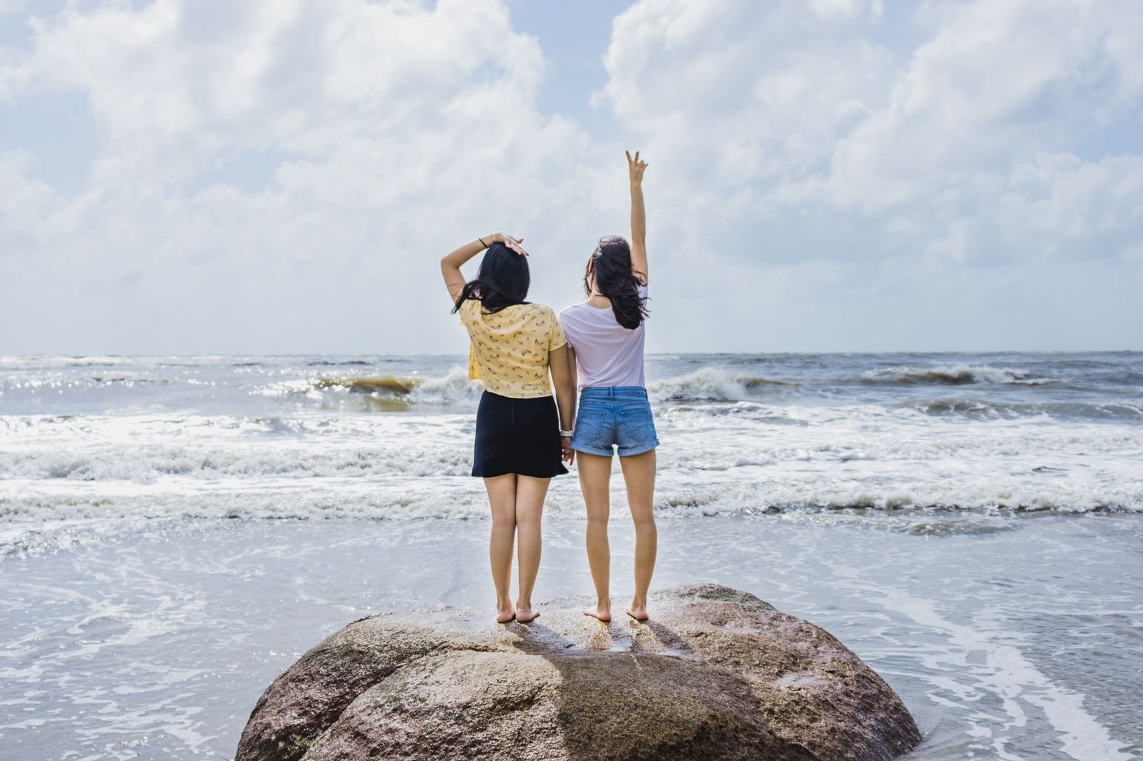 Two women stand on a rock by the beach, enjoying the ocean view.