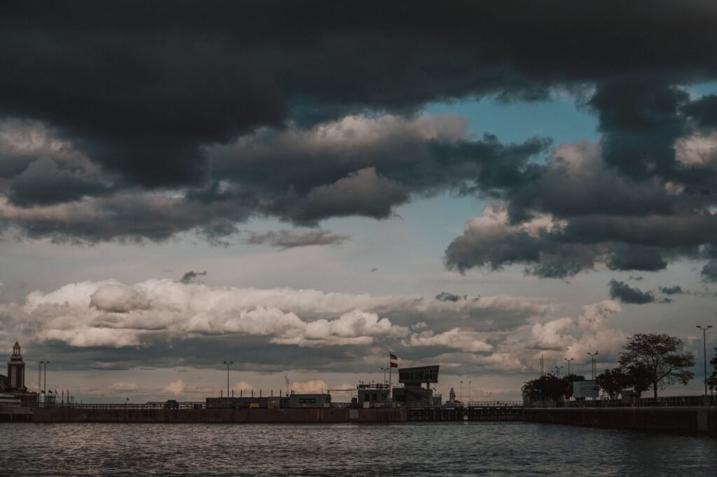 A coastal town under a dramatic sky, featuring dark rain clouds over the sea, shore, and buildings.