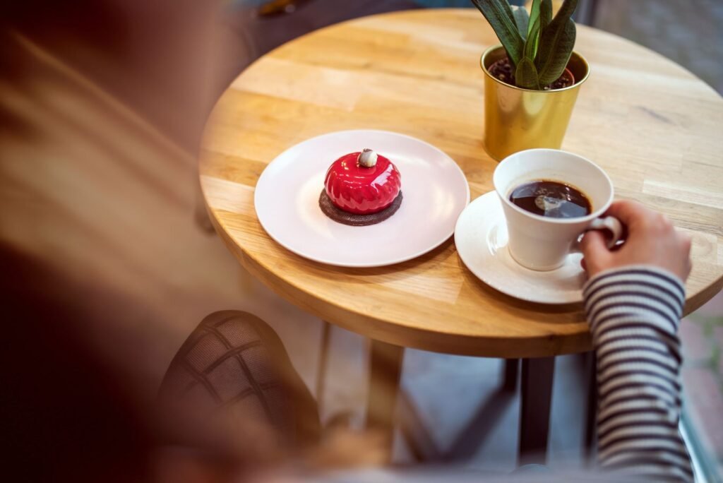 From above of crop anonymous lady in casual outfit drinking aromatic coffee and eating yummy glaze cake while sitting at roun