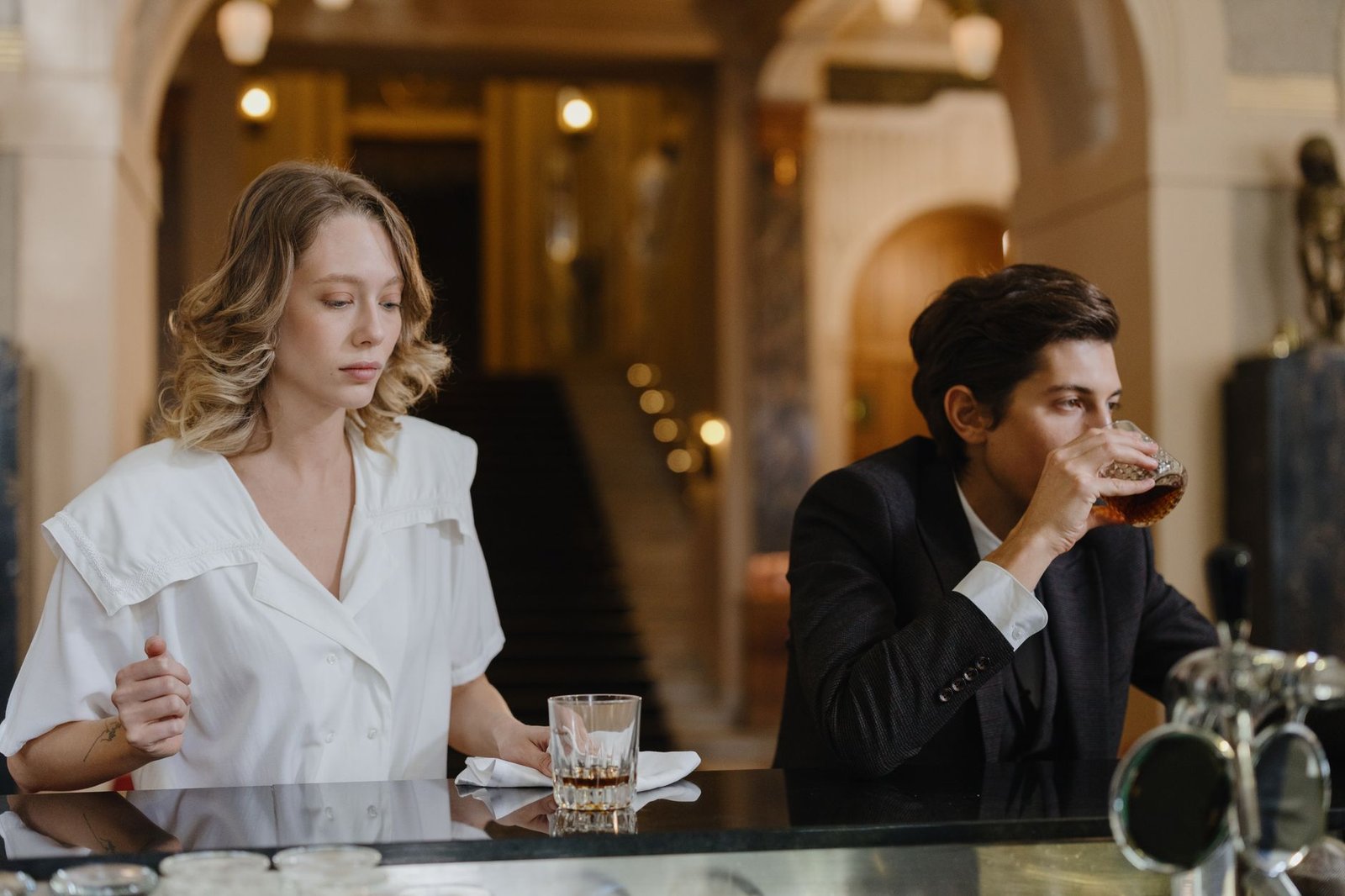 Two adults at a bar enjoying drinks in an elegant, retro-style setting.