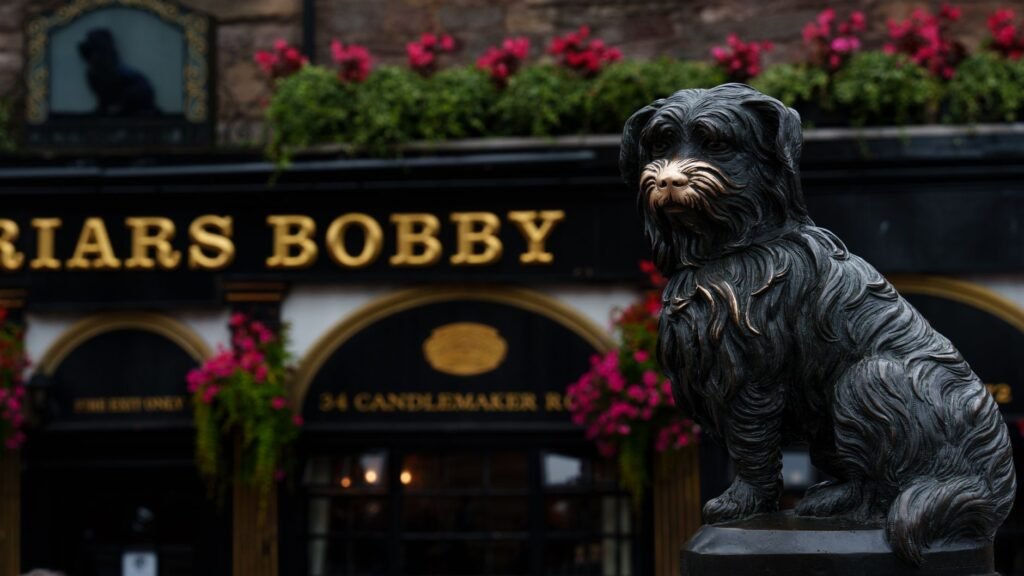 Close-up of Greyfriars Bobby statue with pub background in Edinburgh.