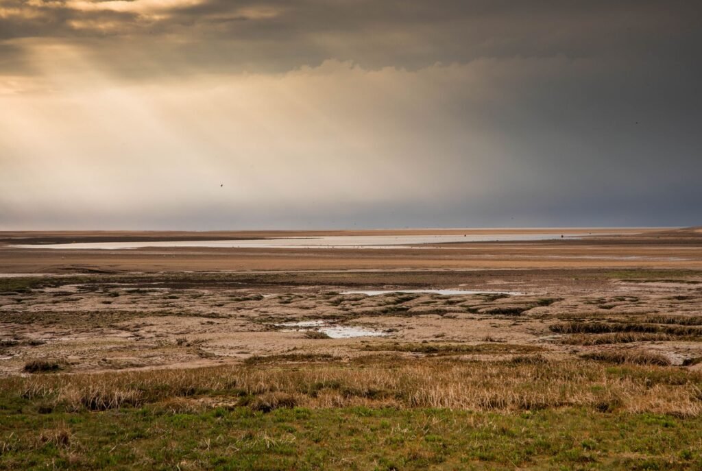 Captivating beach view in Norfolk, England with sun rays breaking through clouds over the coast.