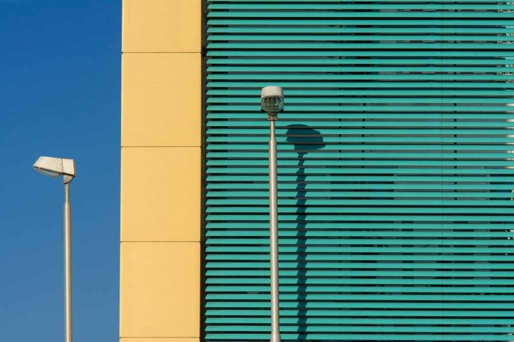A modern building facade with streetlights casting shadows against a clear blue sky.