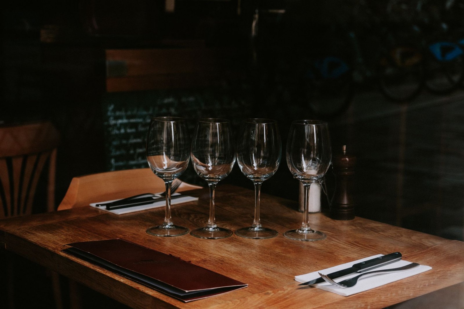 A neatly arranged table with wine glasses and cutlery in a dimly lit restaurant setting.