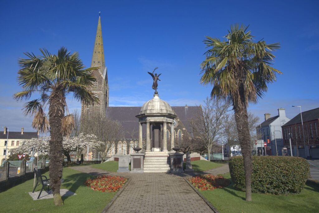 A picturesque war memorial in Lurgan, marked by palm trees and a church in the background.
