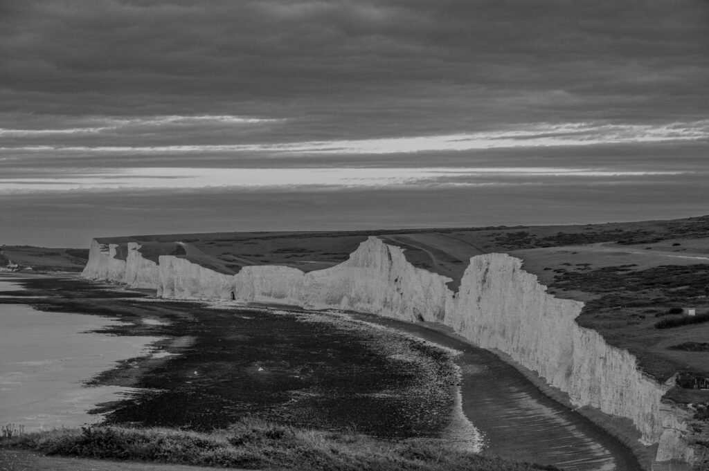 Scenic black and white view of rugged cliffs along a coastline under a dramatic sky.