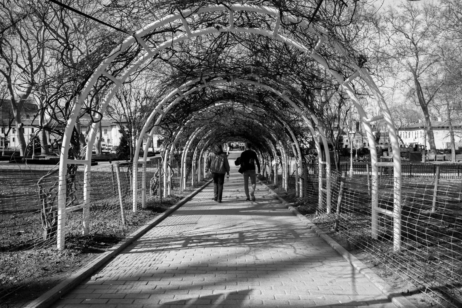 Two people walking under archway in Istanbul park, black and white photo.