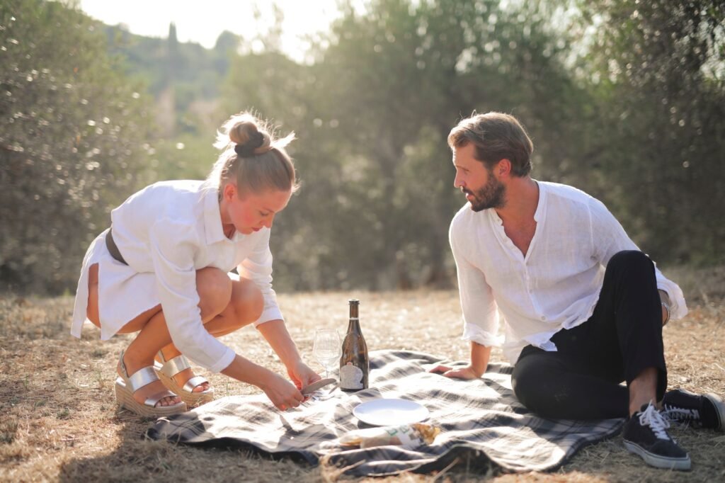A couple enjoying a romantic picnic on a sunny day surrounded by nature, showcasing love and connection.
