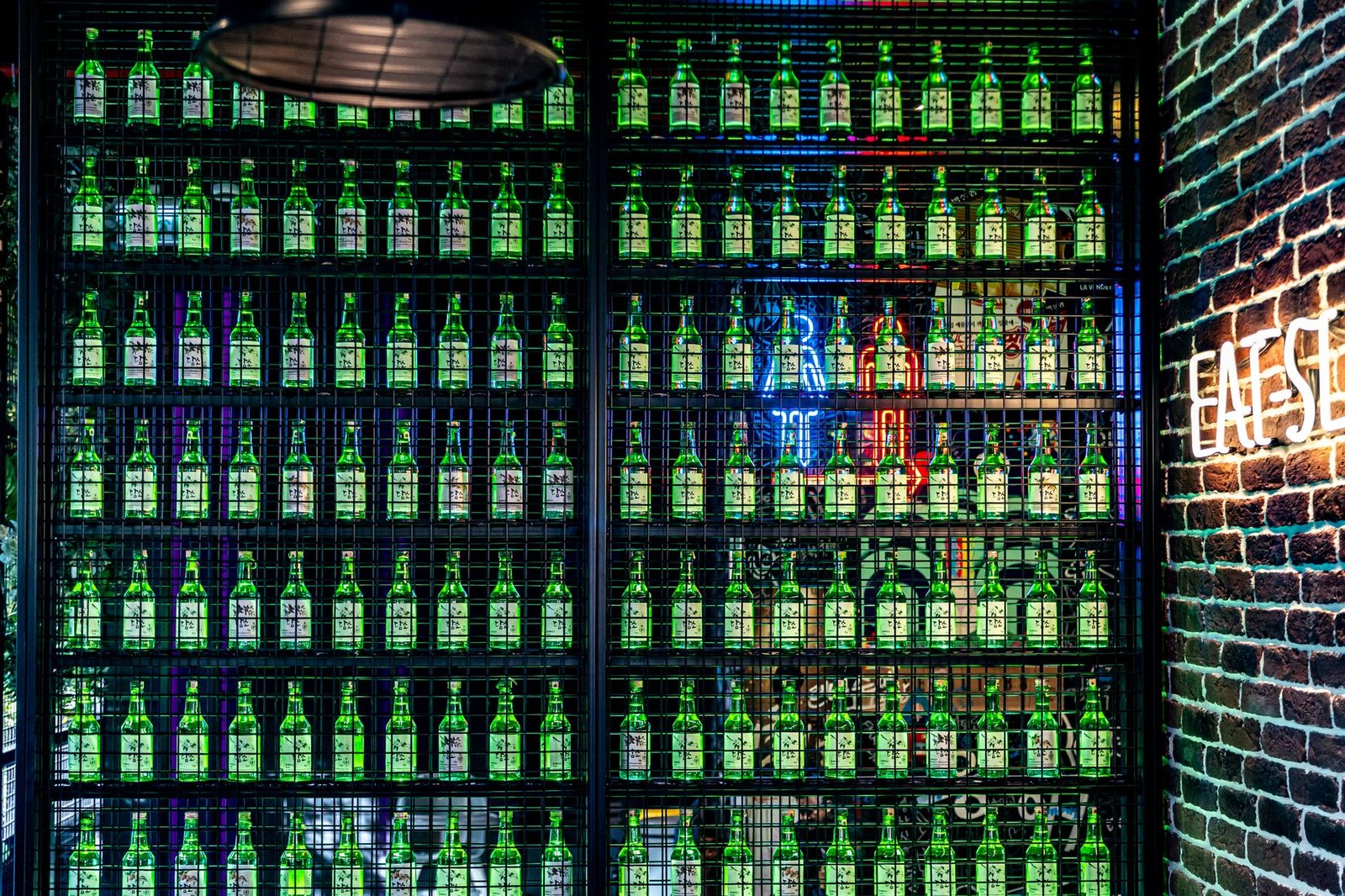 Colorful display of green bottles on a bar wall with neon lights, creating a vibrant and modern atmosphere.