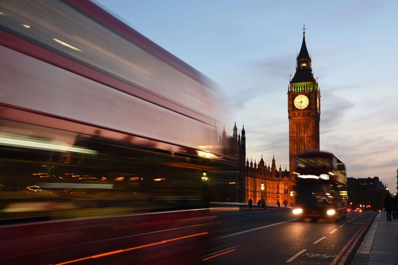 Blurred motion of iconic red buses near Big Ben during twilight in London.